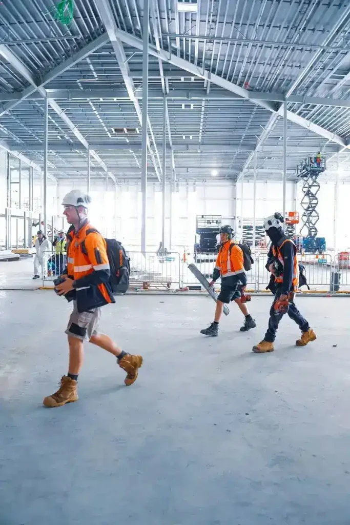 Workers in safety gear cross construction site.