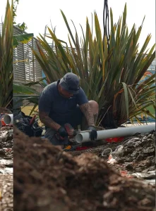 Plumber drills pipe in garden.