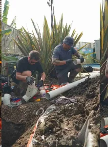 Two people installing PVC pipes outdoors.