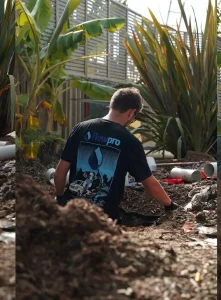 Plumber in trench with pipes.