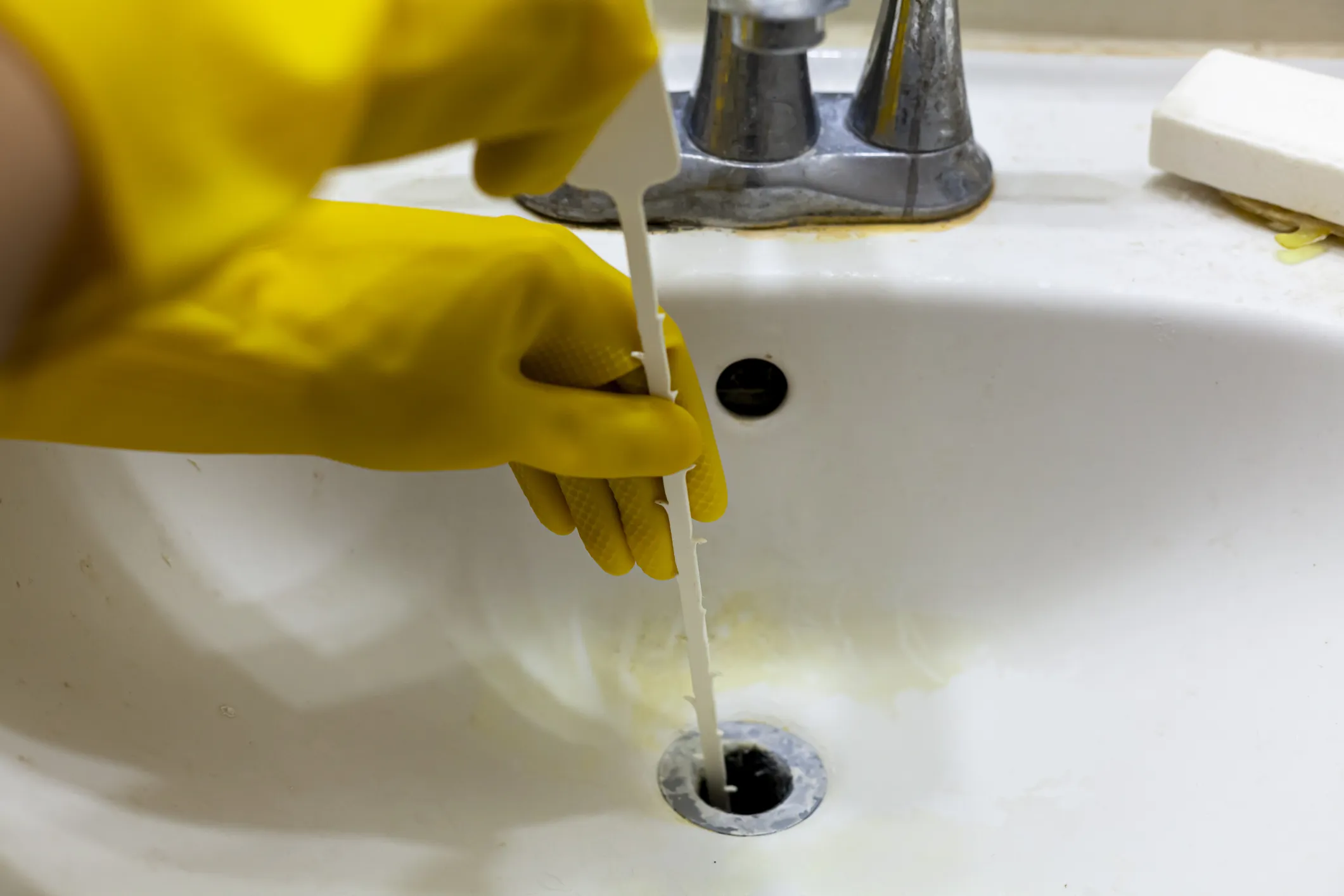 Plumber unclogging sink with drain snake.