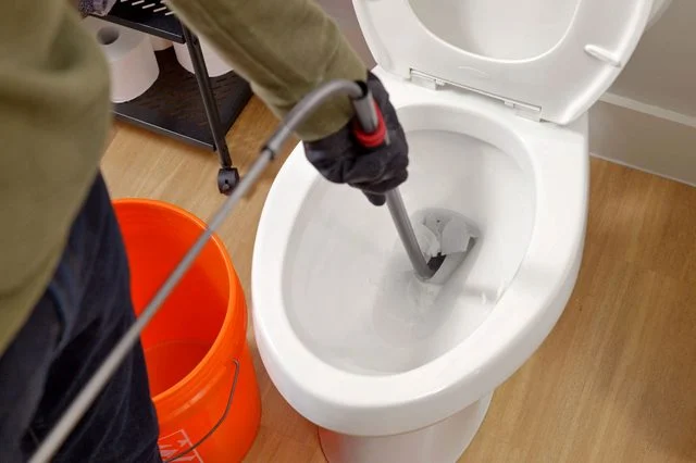 Plumber unclogging toilet with snake.