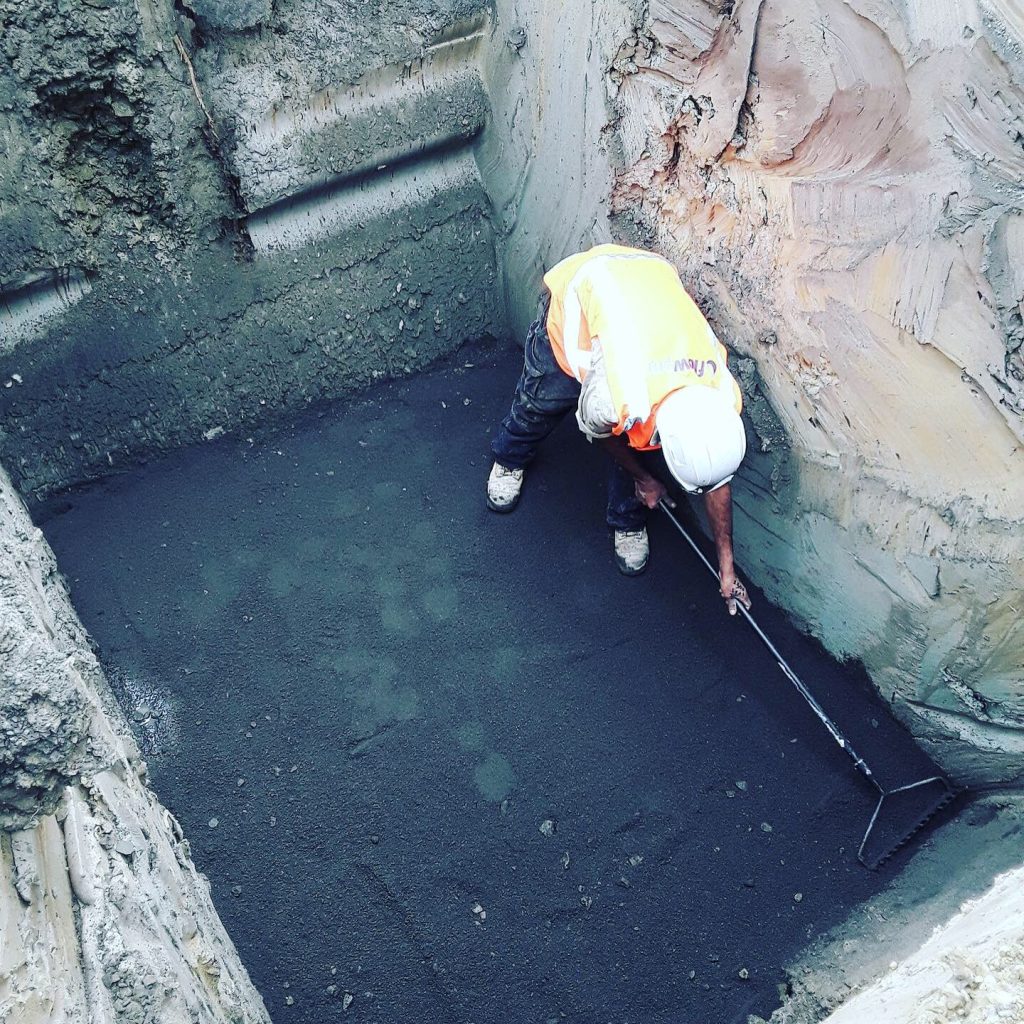 Worker raking material in trench.